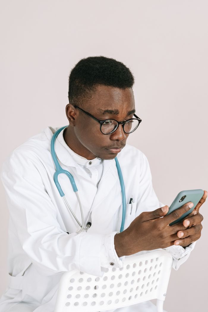Portrait of a focused doctor checking his smartphone while seated indoors.